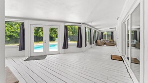 Un patio couvert avec vue sur la piscine, des portes-fenêtres coulissantes et un espace salon extérieur.