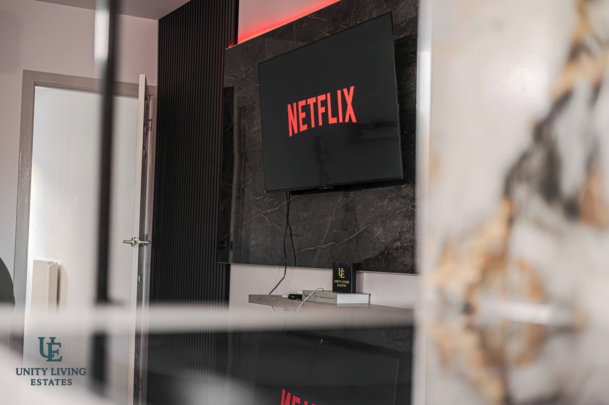 Un intérieur moderne avec un téléviseur fixé au mur affichant le mot « NETFLIX » en lettres rouges, un mur en marbre noir et une cloison en verre.
