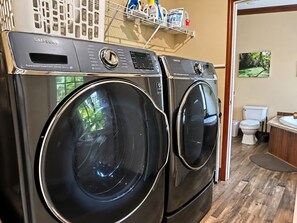 A laundry area with two front-loading washing machines, a shelf with cleaning supplies, and a view of a bathroom with a toilet and sink.