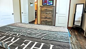 A bedroom with a bed, a dresser, a TV on a stand, and a door leading to another room. - Shelter from the Storm | Weeki Wachee Riverfront Escape (Weeki Wachee)