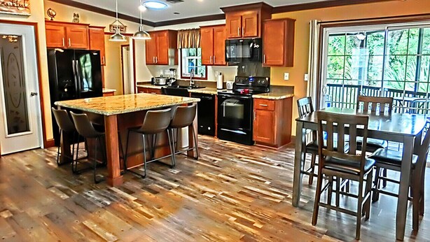 A kitchen with wooden flooring, a central island with chairs, wooden cabinets, a microwave, and a stove. - Shelter from the Storm | Weeki Wachee Riverfront Escape (Weeki Wachee)