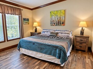 A bedroom with a large bed, two bedside tables, a window with blinds, and a painting on the wall.
