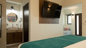 Un dormitorio con cama, televisor montado en la pared, baño con lavamanos y espejo, y vistas al exterior.