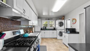 Une cuisine moderne avec des meubles blancs, une cuisinière à gaz, un four à micro-ondes et un lave-linge encastré.