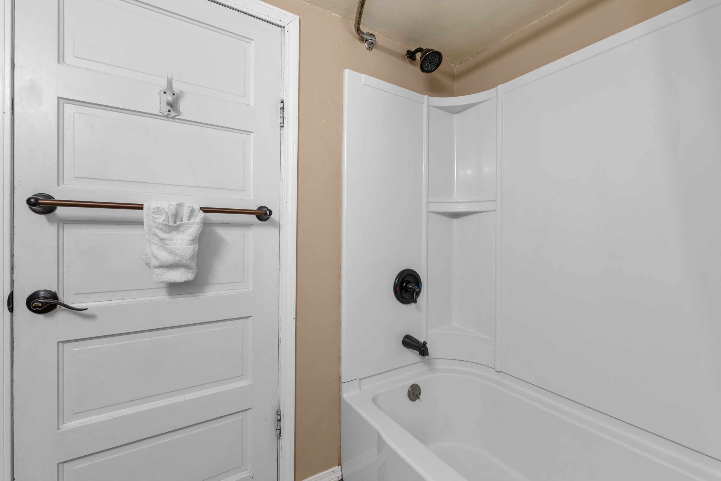 Un baño con una puerta blanca, un perchero con toalla y una bañera blanca.