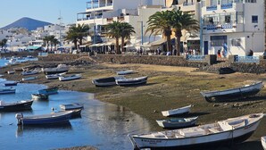 A coastal town with boats docked along the shore, buildings with balconies, and a mountain in the background.