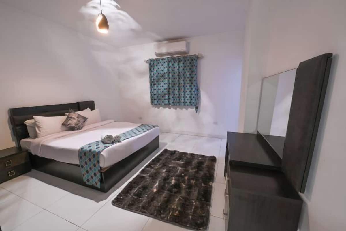 A bedroom with a bed, a rug, a TV, and a window with curtains.