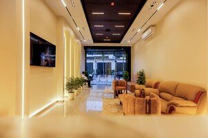A modern lobby with a flat-screen TV, a reception desk, a sofa, and potted plants.