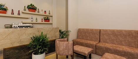 A modern living area with a sofa, a chair, a small table, and a reception desk with potted plants.