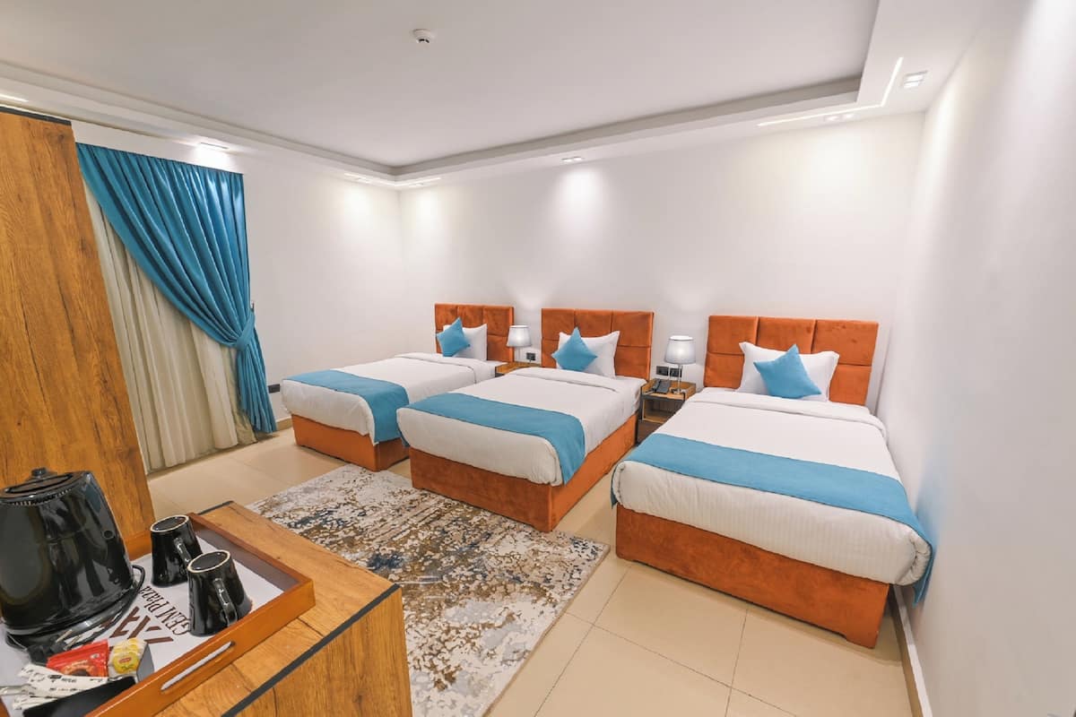 A hotel room with three beds, a wooden desk, and a coffee maker.