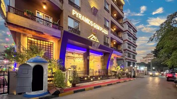 A hotel named 'PYRAMIDS GEM PLAZA' with a modern facade, balconies, and a red carpet entrance.