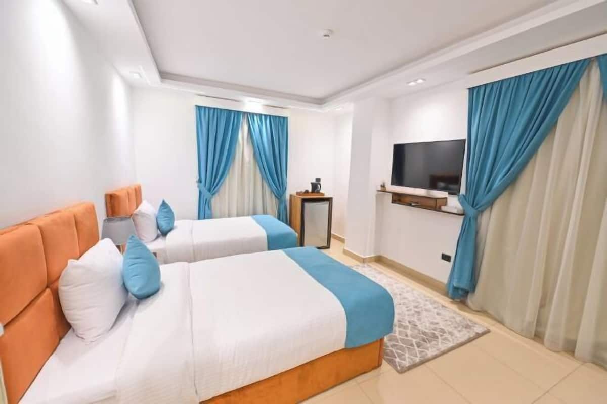 A hotel room with two beds, a TV, and a desk with a lamp.