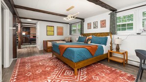 Ein Schlafzimmer mit einem hölzernen Bett, einem roten Teppich mit Muster, einem Nachttisch mit Lampe und einem Fenster mit Vorhängen.