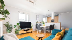 Un salon moderne avec un canapé bleu, un coin repas doté d’une table blanche et une cuisine en arrière-plan.