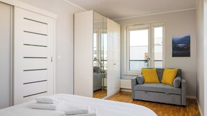 Une chambre à coucher avec un lit, un canapé gris agrémenté de coussins jaunes, une armoire et un grand miroir.