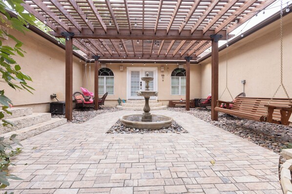 A covered patio area with a central fountain, stone steps, and seating arrangements. - Country Oasis in the City (Mansfield)