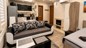 A modern living room with a sofa, a coffee table, a fireplace, and a kitchen area. - Elegant Ground-floor Studio With Covered Terrace and Direct Access to Nature (Smolyan)