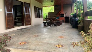 A covered outdoor area with a concrete floor, wooden furniture, and a view of a green landscape. - Green retreat with lake, swimming pool, barbecue and large leisure area surrounded by nature (Canguera)