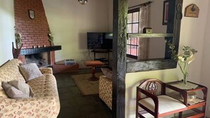 A cozy living room with a sofa, a wooden chair, a television, and a fireplace. - Green retreat with lake, swimming pool, barbecue and large leisure area surrounded by nature (Canguera)