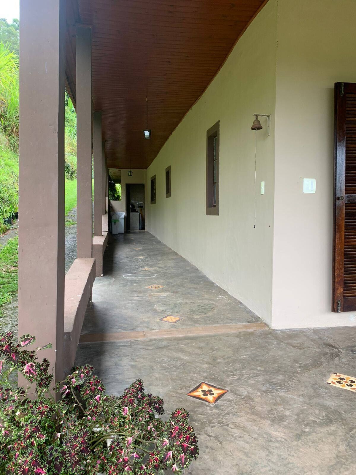 Un corredor cubierto con piso de concreto, vigas de madera y vistas a un jardín exuberante.