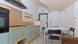 A compact kitchen with a gas stove, a sink, and a refrigerator. There is a dining table with chairs and a sofa. - Balcony in Pollenzo, just minutes from Alba and Bra (Pollenzo)