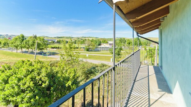 A balcony with a view of a green landscape, a parking area, and a building in the distance. - Balcony in Pollenzo, just minutes from Alba and Bra (Pollenzo)