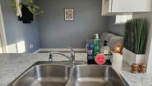 A kitchen with two stainless steel sinks, a countertop, and a wall-mounted television. - Private Sauna Retreat • EV Charger • Quiet Creekside Stay (Duncan)