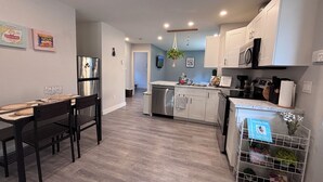 A modern kitchen with white cabinets, stainless steel appliances, and a dining area with a wooden table and chairs. - Private Sauna Retreat • EV Charger • Quiet Creekside Stay (Duncan)
