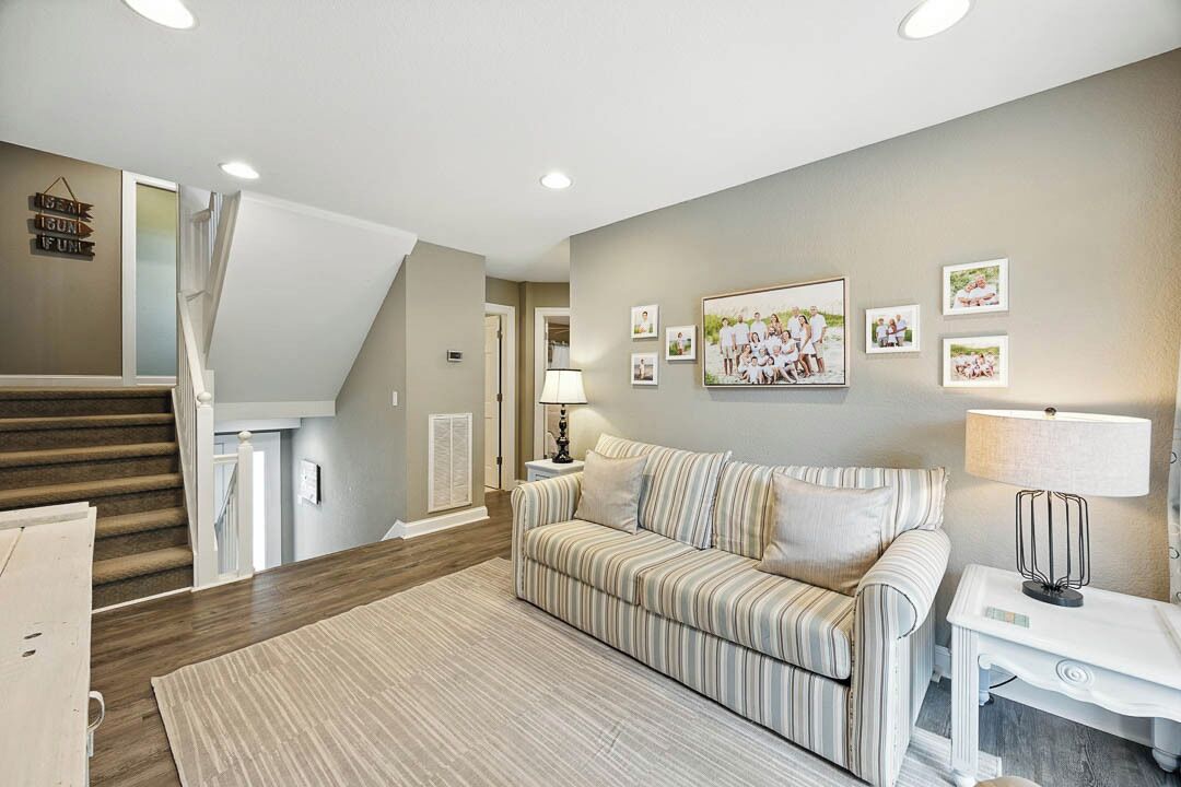 A living room with a striped sofa, a coffee table, and a lamp. There is a staircase in the background and a wall with framed pictures.