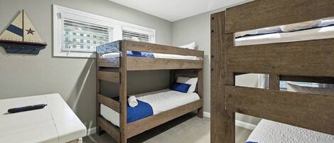 A room with bunk beds, a desk, and a window with blinds.