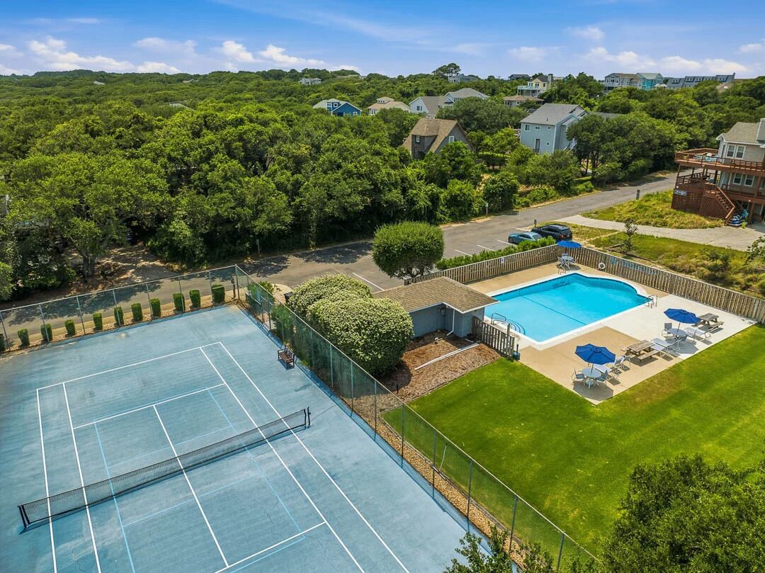 A tennis court, a swimming pool, and a grassy area with lounge chairs.