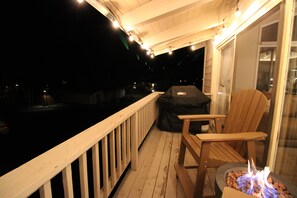 A wooden deck with a barbecue grill and a chair, overlooking a body of water at night. - Cozy 4BR Mountain Escape Sleeps 12 Mountain Escape w'Views (Mammoth Lakes)