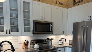 A modern kitchen with white cabinets, a stainless steel refrigerator, a microwave, and a wooden countertop.