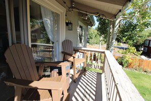 A wooden deck with two Adirondack chairs and a small table, overlooking a backyard with a wooden fence and greenery. - Cozy 4BR Mountain Escape Sleeps 12 Mountain Escape w'Views (Mammoth Lakes)
