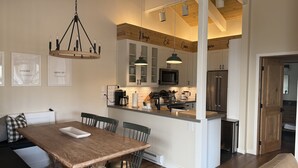 A modern kitchen with white cabinets, a central island, and a dining area with a wooden table and chairs.