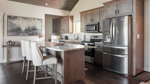 A modern kitchen with wooden cabinets, stainless steel appliances, and a bar area with bar stools. - Luxe | 3 King Suites | Hot Tubs | View | Firepit EV (Banner Elk)