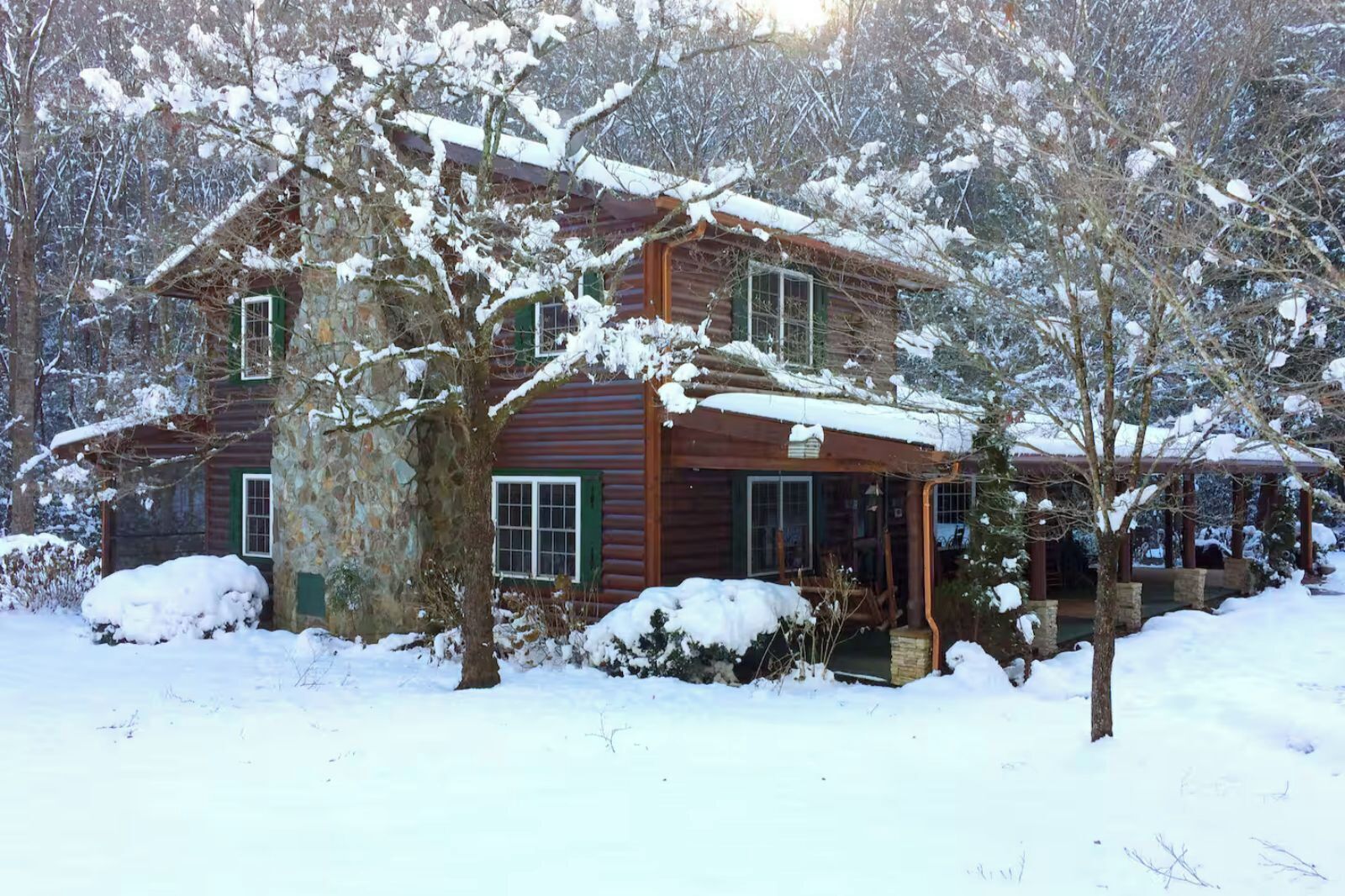 A wooden cabin with a porch, surrounded by snow-covered trees.