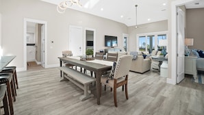 A spacious living area with a dining table, chairs, and a bench. There is a sofa and a TV mounted on the wall.