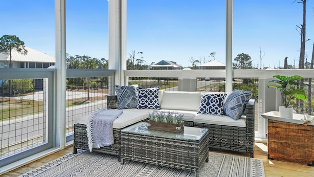 A covered outdoor seating area with wicker furniture, a glass coffee table, and a view of the surrounding landscape.