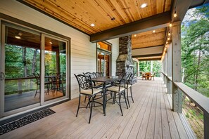 Une terrasse extérieure couverte, dotée d’une table et de chaises, de grandes portes-fenêtres coulissantes et d’une cheminée en pierre.