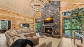 Una sala de estar acogedora con chimenea de piedra, techo de madera y ventanas amplias que dan a un paisaje exterior.