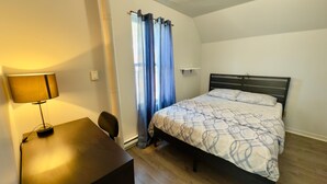 A bedroom with a bed, a desk, a lamp, and a window with curtains.