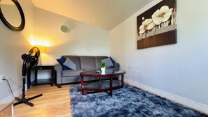 A living room with a grey sofa, a round coffee table, a fluffy rug, a lamp, and a painting on the wall.