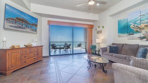 A spacious living area with a large sliding glass door leading to a balcony, a wooden cabinet, a glass coffee table, and a grey sofa.