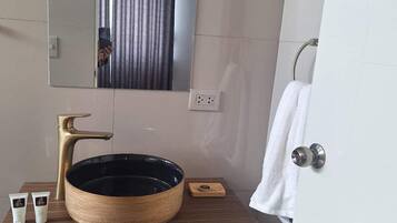 Un baño con tocador de madera, un lavamanos redondo negro, un grifo dorado y un espejo sobre el lavamanos.
