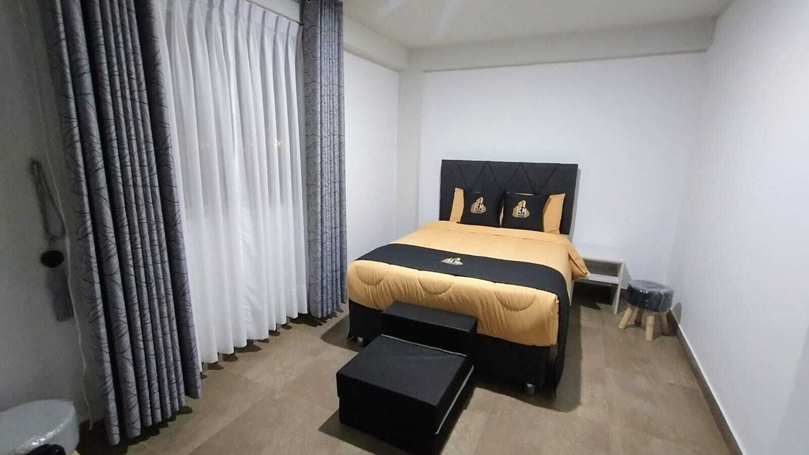 Een slaapkamer met een bed, een nachtkastje, een klein krukje en een bijzettafeltje.