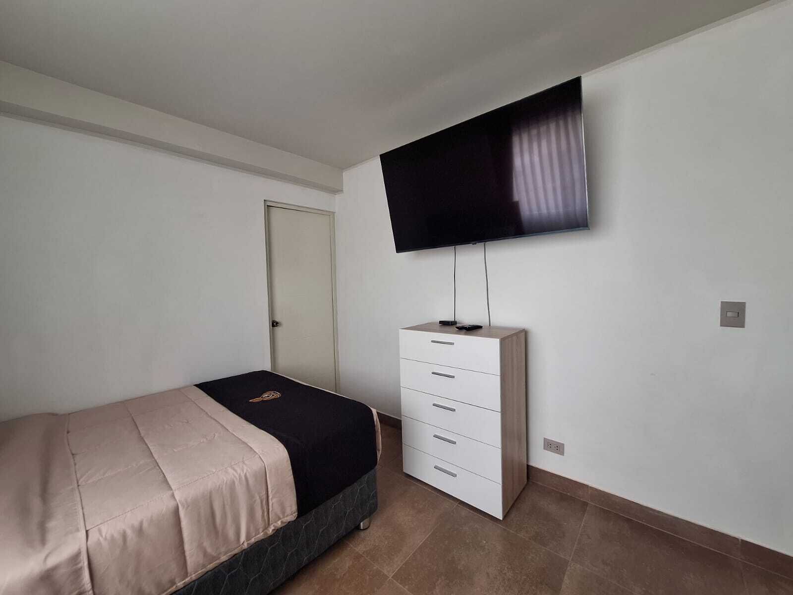 A bedroom with a bed, a dresser, a television mounted on the wall, and a door.