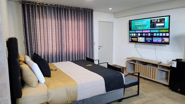 A hotel room with a bed, a TV mounted on the wall, a desk, and a chair. - MAXIMUM COMFORT (Distrito de Chilca)