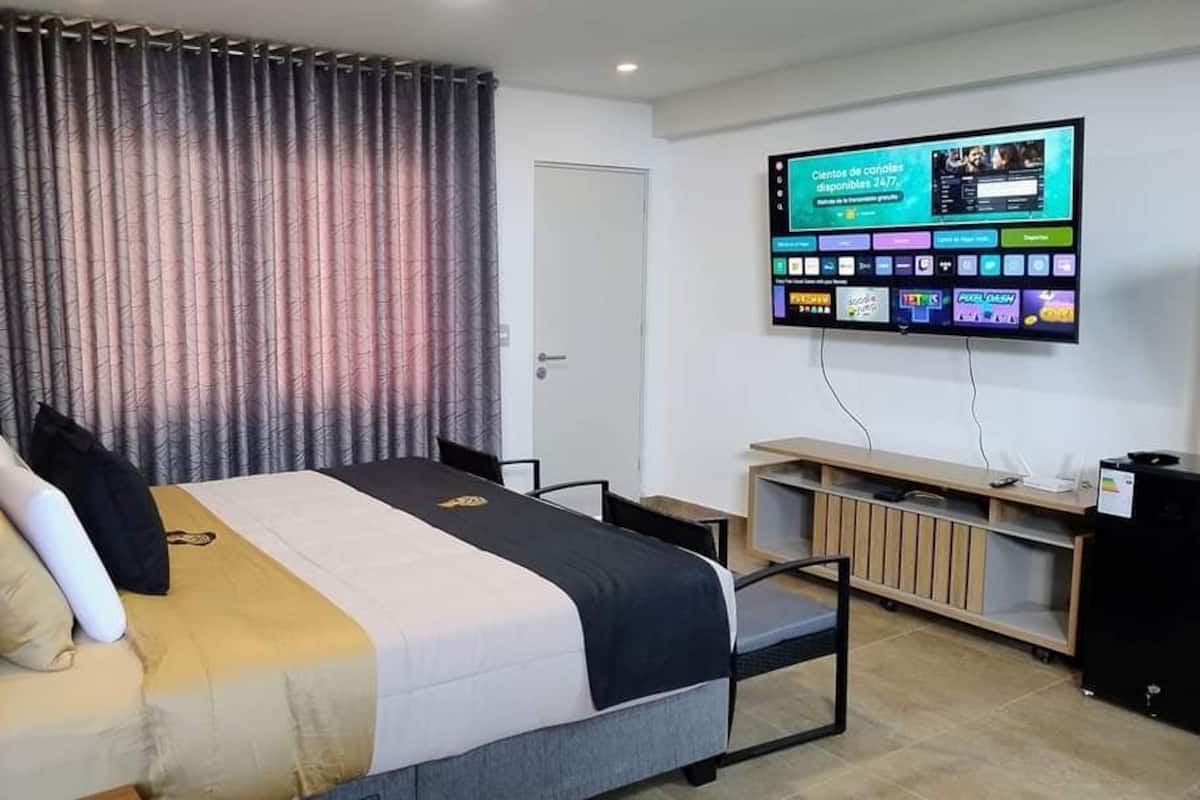 Quarto de hotel com cama, televisão presa à parede, escrivaninha e uma cadeira.