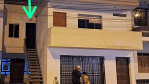 A multi-story building with a staircase leading to the entrance, a gated driveway, and a person walking on the sidewalk. - MAXIMUM COMFORT (Distrito de Chilca)